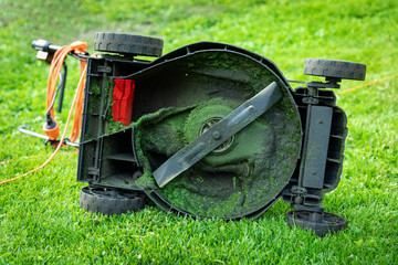 dirty electric lawn mower in green grass at home backyard