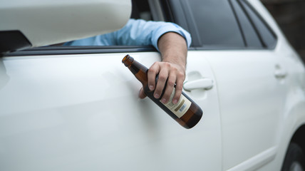 Drunk young man driving a car on the road holding a bottle of beer; Dangerous drunk driving