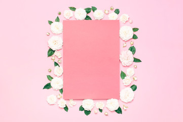 Flowers composition. Pink blank paper, white fresh roses and green leaves on gentle pink background. Flat lay, top view, copy space. Flower card, greeting, holiday mockup. Valentine's Day background