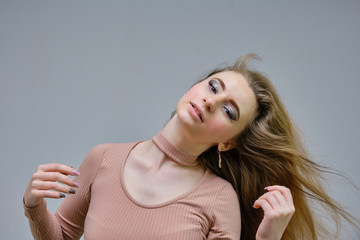 A photo portrait of a beautiful woman girl on a light gray background with long beautiful hair in a pink sweater and blue jeans is standing right in front of the camera and smiling.