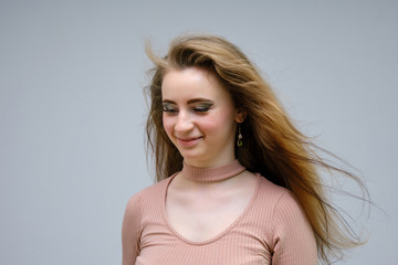 A photo portrait of a beautiful woman girl on a light gray background with long beautiful hair in a pink sweater and blue jeans is standing right in front of the camera and smiling.