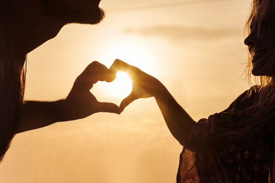 couple showing heart shape with their fingers on the sunset