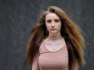 Naklejka premium A portrait of a beautiful girl woman on a dark gray background with long beautiful hair in a pink sweater and blue jeans is standing right in front of the camera and smiling.