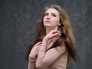 Fototapeta premium A portrait of a beautiful girl woman on a dark gray background with long beautiful hair in a pink sweater and blue jeans is standing right in front of the camera and smiling.