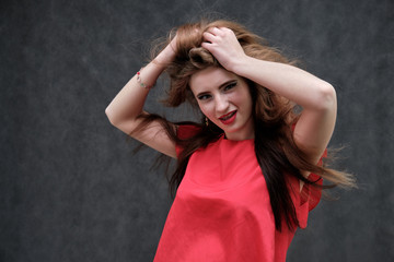 Photo portrait of a beautiful girl of the woman on a dark gray background with long beautiful hair in a red sleeveless jacket standing right in front of the camera and smiling.