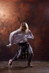 Fototapeta na wymiar Photo of young dancing blonde girl in ripped jeans and sneakers on brown background