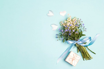 A bouquet of lily of the valley and forget-me-nots with gift box on a blue background.