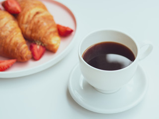 Morning cup of coffee and breakfast plate with croissants and strawberries