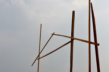 Brown wooden poles are seen from below. they are vertical, with a few forming an A shape of a roof. The sky is overcast with grey clouds.
