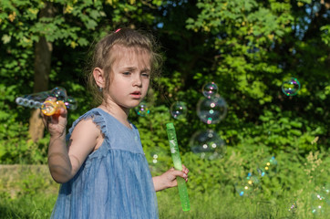 Little charming girl blows soap bubbles