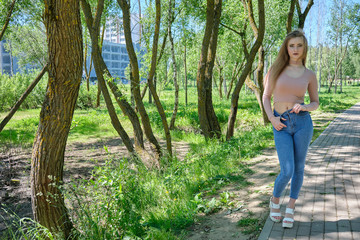 Naklejka na ściany i meble Photograph of a beautiful girl woman on nature in the park with long flowing beautiful hair in a pink sweater and blue jeans on a sunny day is standing right in front of the camera and smiling.
