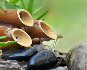 close on a bamboo fountain with water flowing on black stones on green background