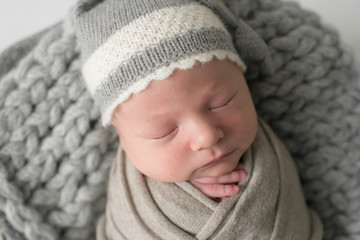 Sweet newborn baby sleeps in a basket. Beautiful newborn boy in a grey knitted hat