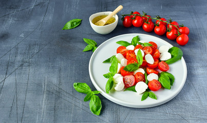 Italian Caprese salad: red tomatoes, fresh organic mozzarella and Basil, Italian cuisine. Healthy lunch. Top view on gray stone table