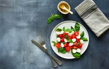 Italian Caprese salad: red tomatoes, fresh organic mozzarella and Basil, Italian cuisine. Healthy lunch. Top view on gray stone table