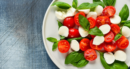 Italian Caprese salad: red tomatoes, fresh organic mozzarella and Basil, Italian cuisine. Healthy lunch. Top view on gray stone table