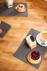 Top view photo of cake with tasty biscuit near different mini cakes on a wooden table in a coffee shop