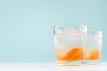Detox beverage with oranges liquor and mineral water, ice cubes on white wood table, pastel green background.