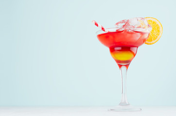 Summer cold alcohol striped cocktail with oranges juice, straw, ice cubes in luxury glass on pastel blue background, copy space.