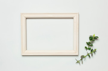 White wooden photo frame and spring green twigs of plants on gray background. Flat lay top view copy space. Stylish minimal composition, artwork mockup, picture frame, home decoration
