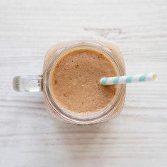 Mason glass jar mug filled with banana apple smoothie on a white wooden background, top view. Flat lay, from above, overhead.