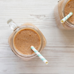 Banana apple smoothie in glass jars over white wooden background, overhead view. Flat lay, from above, top view.