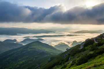 Fantastic view of mountain valley covered with low white puffy like snow clouds stretching to foggy...