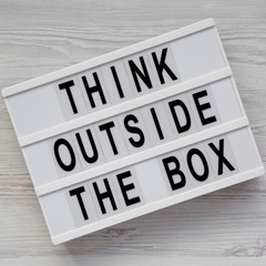 Modern board with 'Think outside the box' words on a white wooden background, top view. Flat lay, overhead, from above. Close-up.