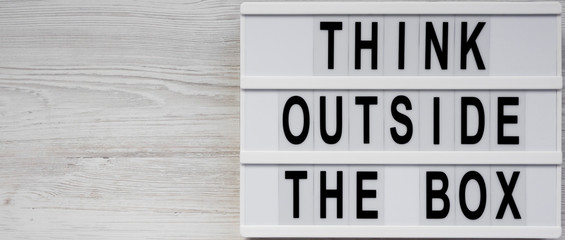 'Think outside the box' words on a modern board on a white wooden surface, top view. Flat lay, overhead, from above. Copy space.