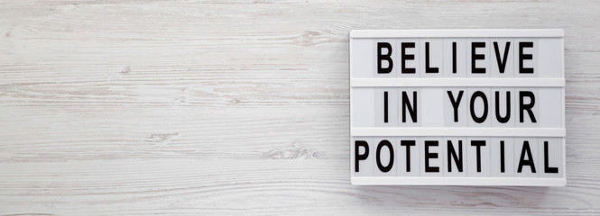 Top view, 'Believe in your potential' words on a lightbox on a white wooden surface. Flat lay,...