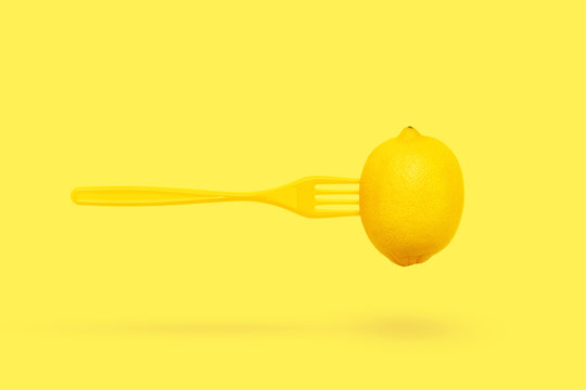 lemon and plastic fork levitation on pastel yellow background. Minimal summer concept. Absrtact trendy creative design.
