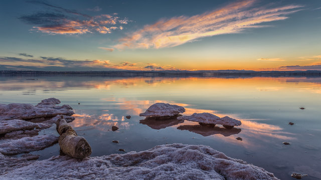 A tree trunk lies in the salt lake. The lagoon of Torrevieja in Spain after sunset with beautiful reflections in the water. The salt forms interesting shapes, like a mushroom.
