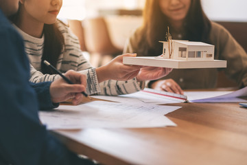 Fototapeta premium Group of an architect holding and discussing about an architecture model with shop drawing paper on table in office