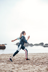 Beach workout. Vertical photo of strong sporty disabled woman with prosthetic leg is running on the beach and doing morning workout.