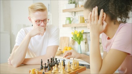 Young blonde man is playing chess with african american young woman