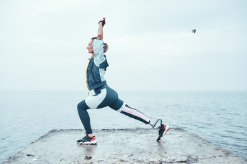 Yoga for health. Sporty disabled athlete woman in sportswear with prosthetic leg standing in yoga...