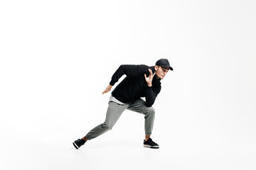 Fototapeta na wymiar Handsome young man wearing a black sweatshirt, gray pants and a cap dancing street dances on a white background