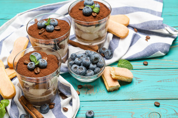 Classic tiramisu dessert in a glass with blueberries on blue wooden background