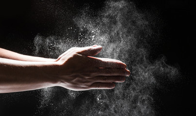 Fototapeta na wymiar Powdery flour flying into air as man in black chef outfit wipes off his hands