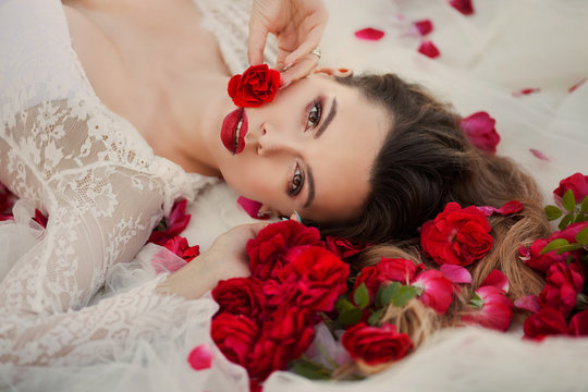 Valentine's Day. Loving girl. The girl in a red dress lying on the floor in the petals of red roses.
