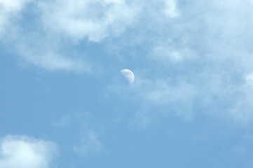 The moon in the blue sky is partially hidden by the clouds, the daytime shot. Cloudscape.