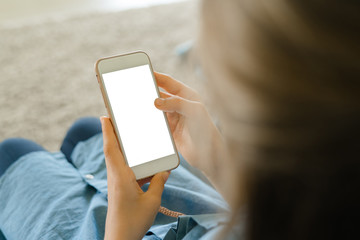 Teenage girl in a blue dress sitting on an armchair while holding a smart phone with a blank screen in the hands. Young girl using scrolling on social media, youth addiction
