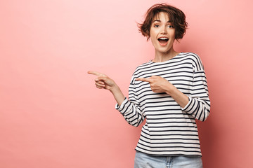 Excited shocked surprised beautiful woman posing isolated over pink wall background pointing.
