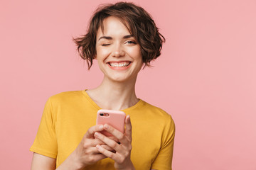Happy young beautiful woman posing isolated over pink wall background using mobile phone.