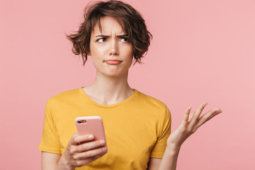 Confused young beautiful woman posing isolated over pink wall background using mobile phone.