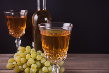Two glasses of white wine, bottle and bunch of grapes standing on a wooden table