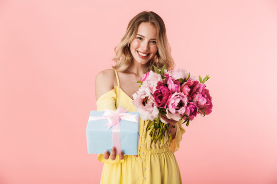 Amazing Young Blonde Woman Posing Isolated Over Pink Wall Background Holding Flowers Holding Present Gift Box.