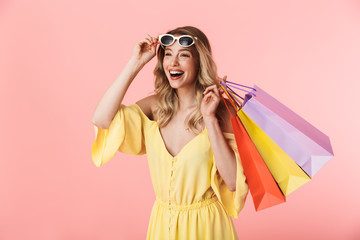 Beautiful shocked young blonde woman posing isolated over pink wall background holding shopping...
