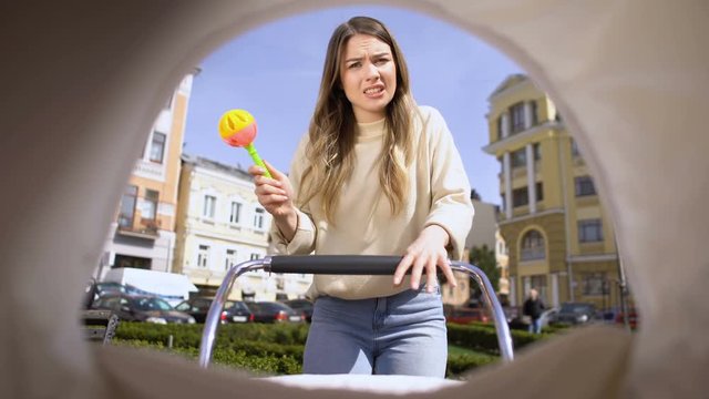Nervous mother with rattle toy swinging carriage, trying to calm down infant