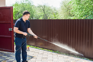 Gun water hose nozzle sprayer. A man's hand holds a black gun watering hose with splash. Man...
